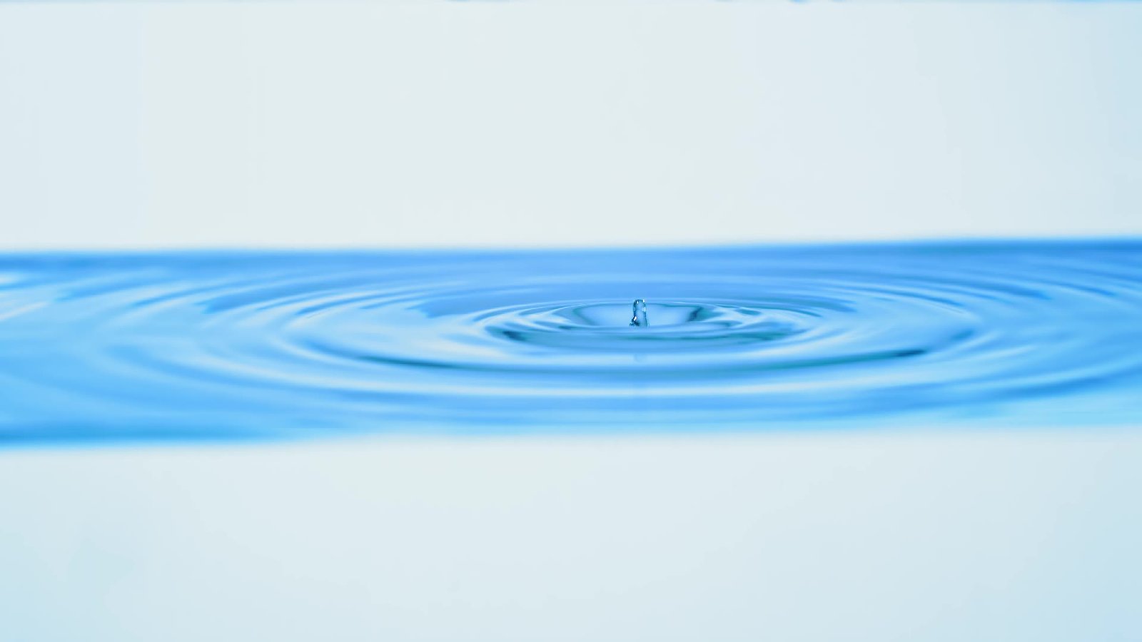 Real blue water droplets creating ripples, filmed from a low side angle